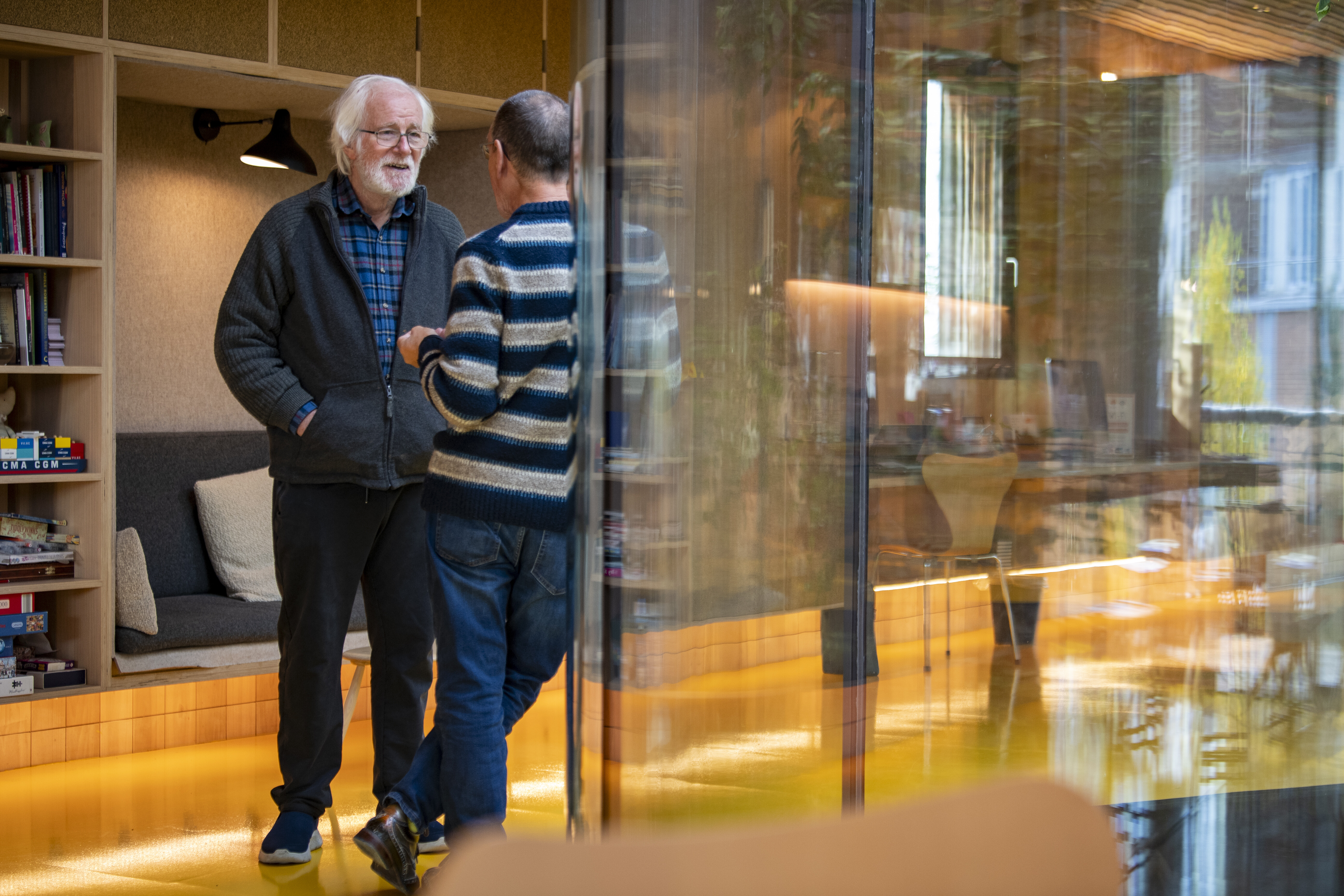 Two men engaged in conversation inside a cozy, modern room with warm lighting.
